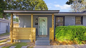 A residential house with a grey brick exterior, a green door, and a wooden porch with benches. - Tailgaters paradise, grill, game room, sunroom-large backyard! (Columbia)