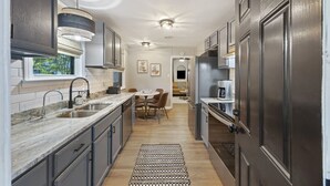 A modern kitchen with dark cabinetry, a marble countertop, and a dining area with a round table and chairs. - Tailgaters paradise, grill, game room, sunroom-large backyard! (Columbia)