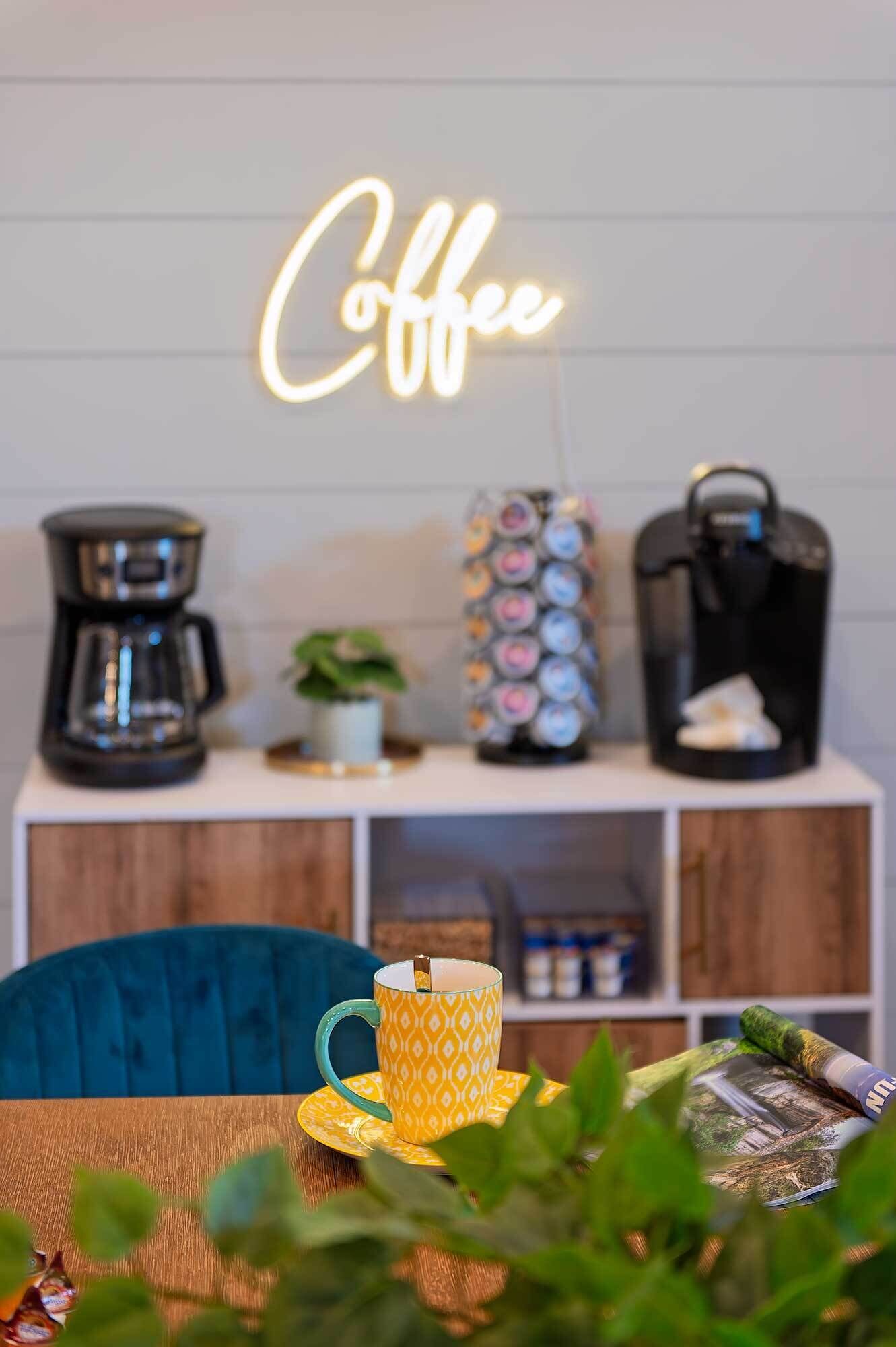 Een setting met koffie als thema, met een neonbord, een koffiezetapparaat, een waterkoker en een mok op een tafel.