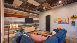Una sala de estar moderna con un sofá azul, un panel de pared de madera y un televisor de pantalla plana montado sobre un mueble de madera.