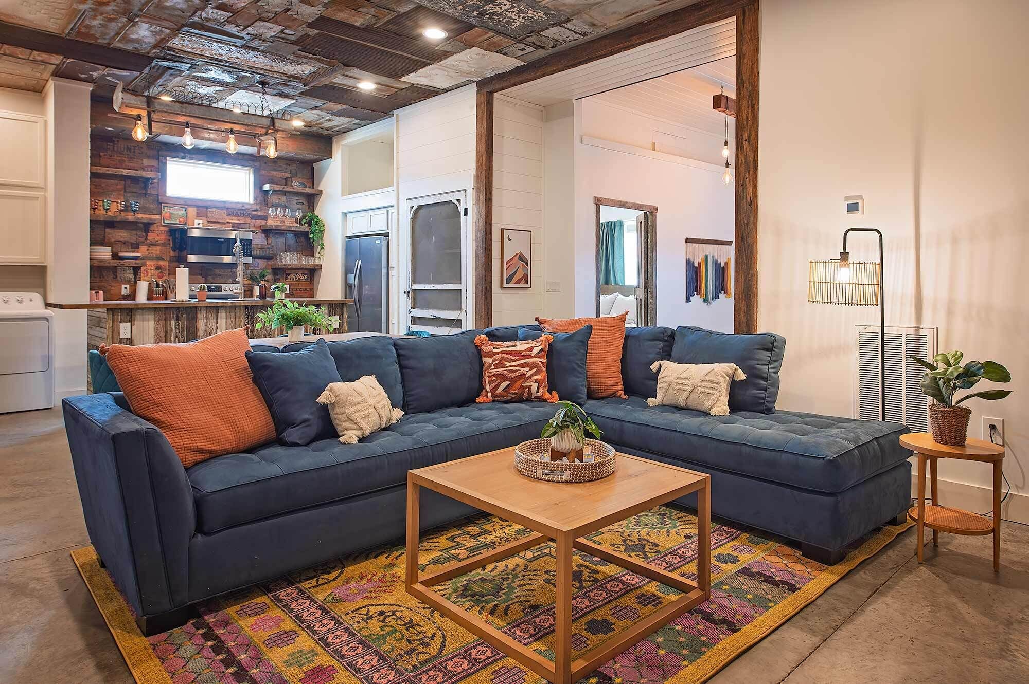 A modern living room with a dark blue sectional sofa, a wooden coffee table, and a colorful rug.