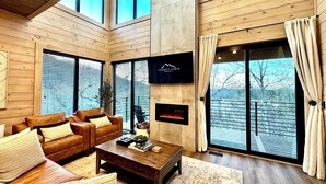 A modern living room with a wooden ceiling, large windows, a fireplace, and a television. - Mountain High Rooftop Cabin Pigeon Forge NEW Indoor Pool Hot Tub Sleeps 15 (Pigeon Forge)
