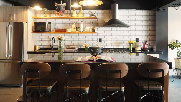 Una cocina moderna con una isla central, taburetes de bar, un refrigerador de acero inoxidable y una campana extractora negra.