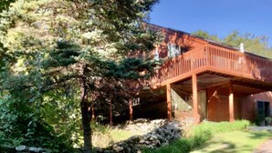 A rustic cabin with a stone foundation, a wooden deck, and a red roof. - Seapowet suite (Tiverton)