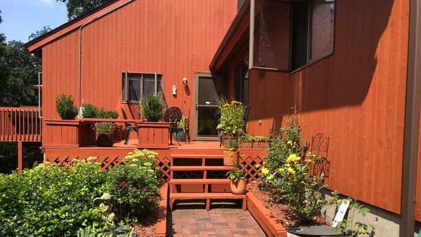 A red wooden house with a front porch, steps leading to the door, and a garden with various plants and flowers. - Seapowet suite (Tiverton)