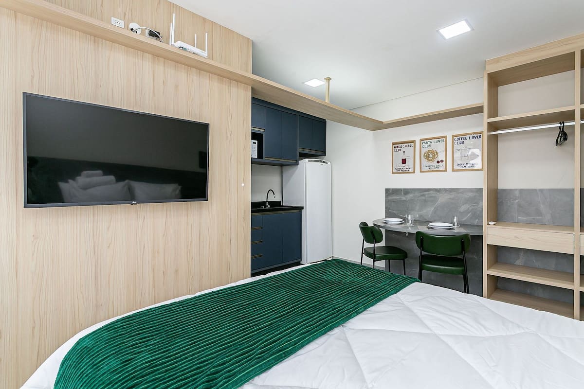 Kompakti hotellihuone, jossa on sänky, televisio, pieni keittiö ja ruokailutila.