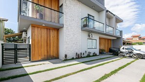 A modern two-story house with a stone facade, large wooden doors, and a balcony with a potted plant. - Nice Godrop Campeche (Florianópolis)