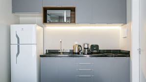 A compact kitchenette with a refrigerator, microwave, coffee maker, and a small countertop. - Nice Godrop Campeche (Florianópolis)