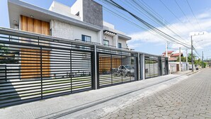 A modern house with a metal fence, a paved driveway, and a clear sky. - Nice Godrop Campeche (Florianópolis)