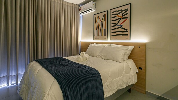 A neatly made bed with a white comforter and a dark blue throw blanket, a wooden headboard, and two abstract art pieces on the wall. - Nice Godrop Campeche (Florianópolis)