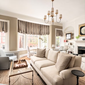 A living room with a beige sofa, a glass coffee table, and a chandelier. - Charming 4-Bedroom Home in Historic Old Town - minutes from King St, DC, & Metro (Alexandria)