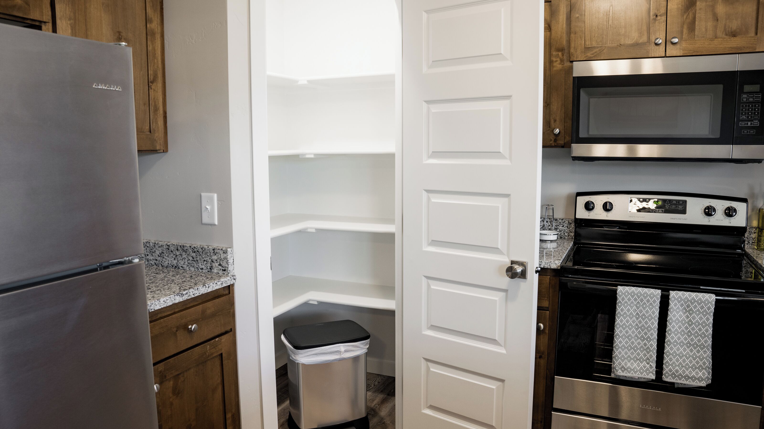 A kitchen with a stainless steel refrigerator, a microwave, and a stove. There is a trash can and a door leading to a pantry.