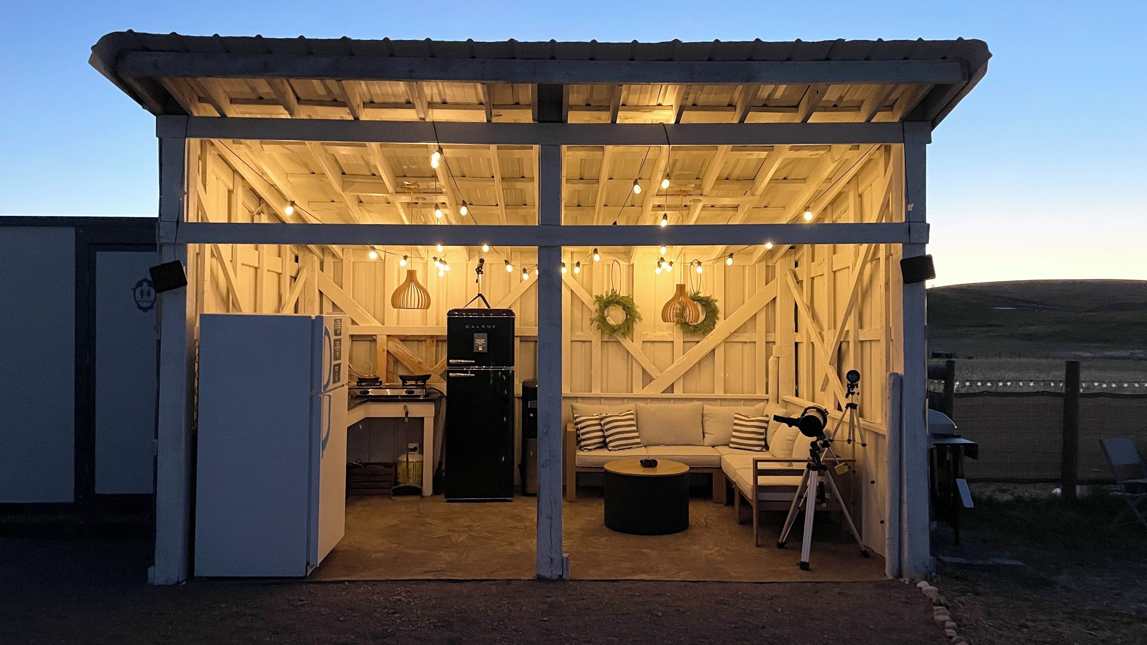 A rustic cabin with a wooden interior, a kitchenette, a sofa, and a telescope.