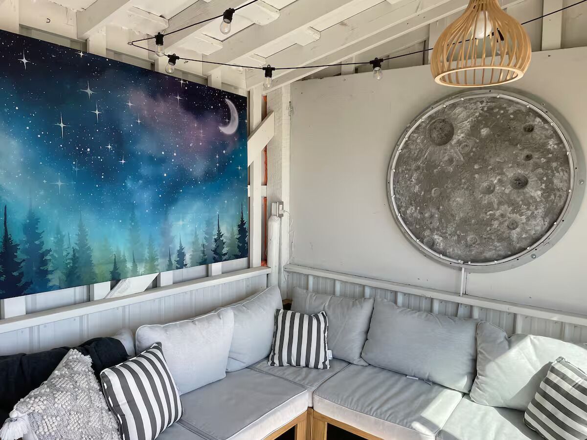 A cozy seating area with a starry night mural, a round moon-like wall decoration, and a wooden pendant light.