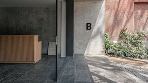 A reception area with a wooden reception desk, a concrete wall with a letter 'B', and a small plant by the wall. - Indigo Veracruz Roma norte Apt 1B I 1B (Mexico City)
