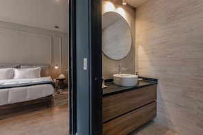 Un dormitorio moderno con una cama, una mesita de noche y un espejo redondo sobre un tocador de madera con un lavabo.