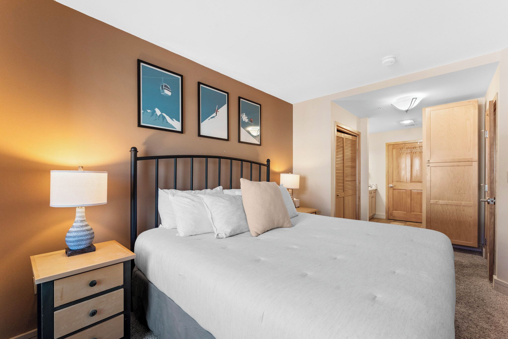 Une chambre à coucher avec un lit, des tables de chevet, une lampe et des tableaux encadrés accrochés au mur.