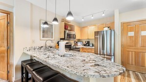 A kitchen with a marble countertop, stainless steel appliances, wooden cabinets, and pendant lighting. - Sm8272-2 (Keystone)