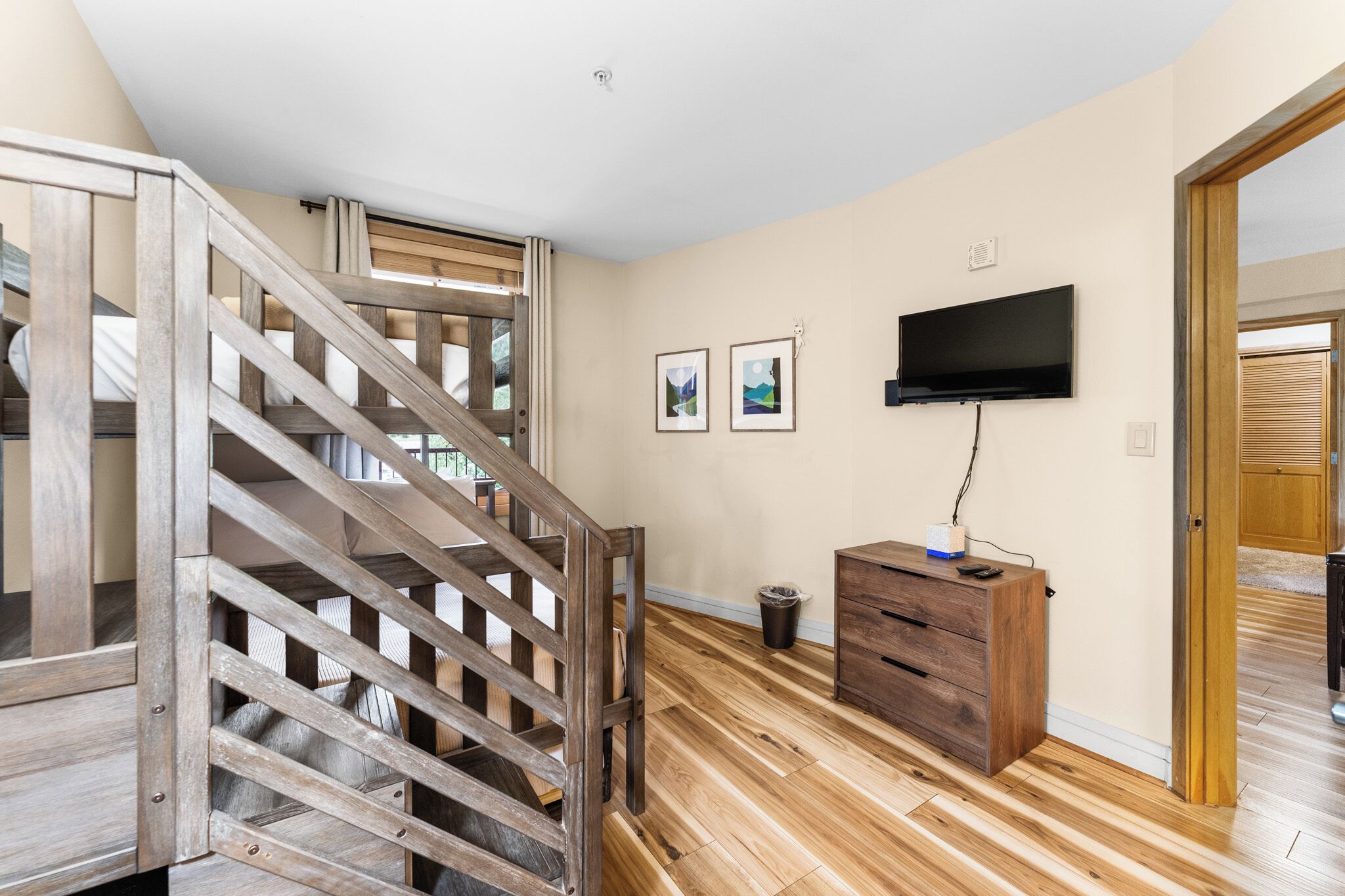 A room with a wooden staircase, a flat-screen TV mounted on the wall, and a wooden cabinet.