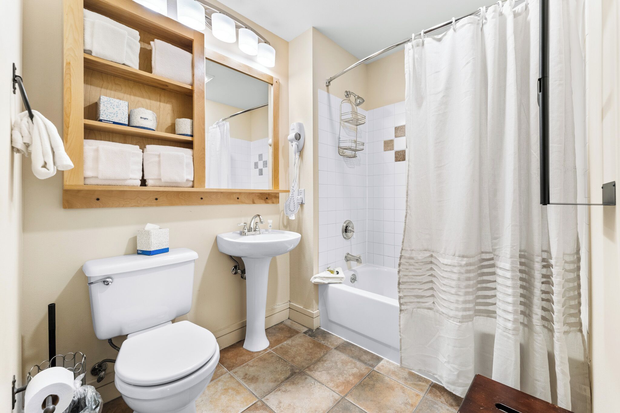 A bathroom with a toilet, sink, shower, and a shelf with towels.