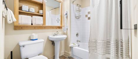A bathroom with a toilet, sink, shower, and a shelf with towels.