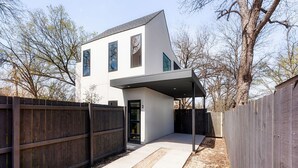 A modern two-story house with a covered patio, a wooden fence, and a driveway. - Modern East Austin Hideaway - Stylish - Walkable (Austin)