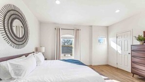 Ein modernes Schlafzimmer mit einem großen Bett, einer runden Wanddekoration, Blick ins Freie durch ein Fenster und Holzboden.