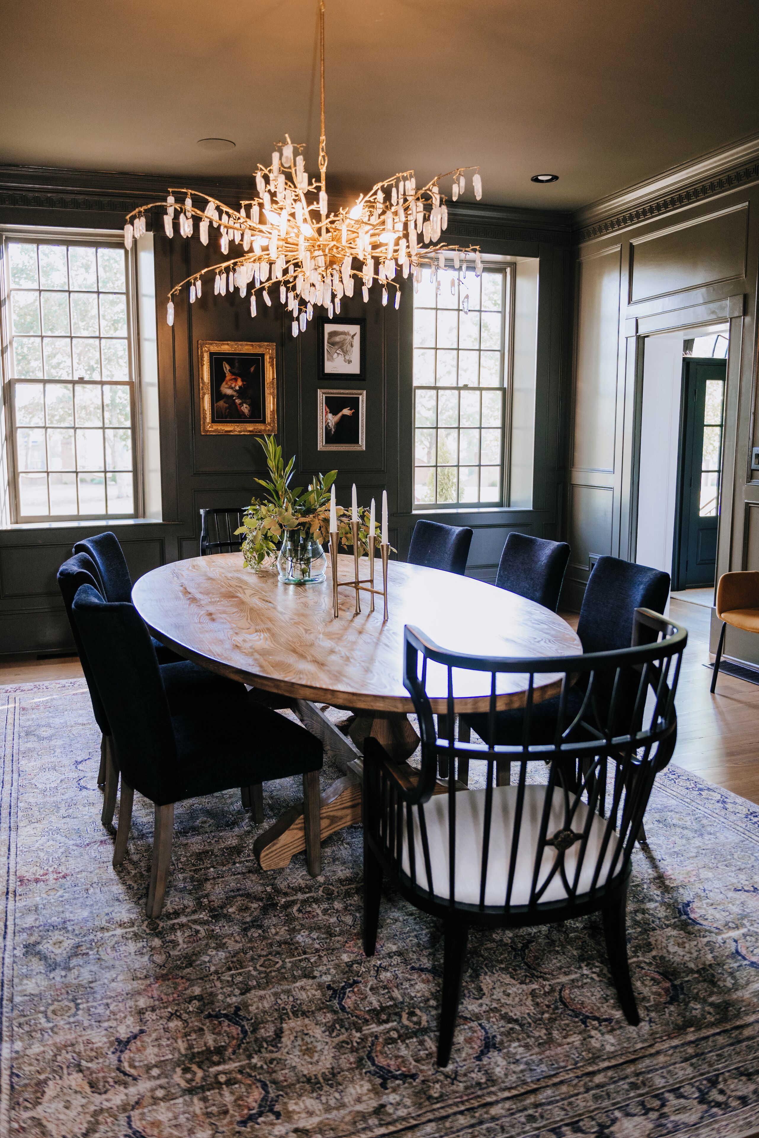 A dining room with a round table, black upholstered chairs, a chandelier, and framed artwork on the walls.