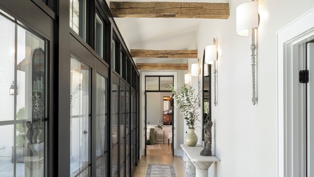 Un pasillo con techo de madera, ventanas amplias y un tapete estampado.