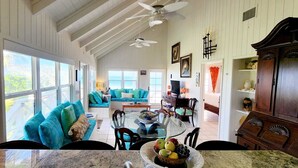 A spacious living area with a large window, a blue sofa, a dining table with chairs, and a ceiling fan.