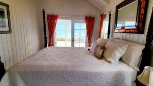 A bedroom with a large bed, a nightstand, a mirror, and a window with curtains.