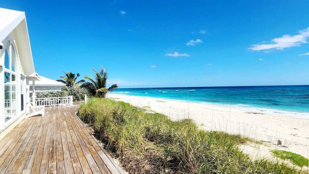 A beach house with a wooden deck, white exterior, and a view of the ocean.