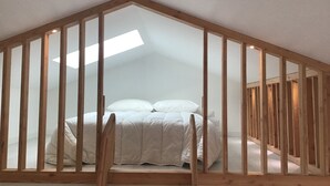 A loft bedroom with a sloped ceiling, wooden beams, a skylight, and a bed with white bedding.