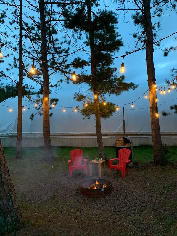 A tented outdoor area with string lights, a fire pit, and red chairs.