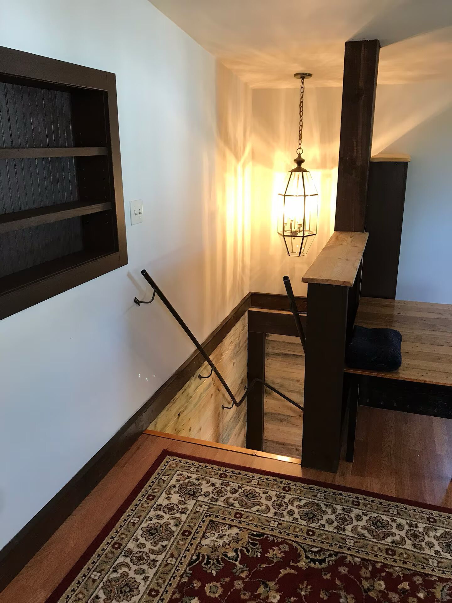 A staircase with a wooden handrail, a hanging lantern, and a patterned rug on a wooden floor.