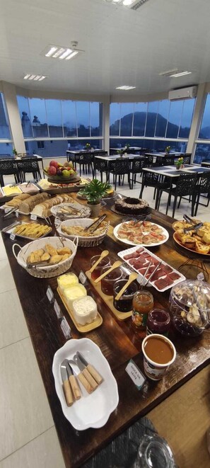 Un buffet con diversi piatti e utensili, disposti su un lungo tavolo in una stanza con ampie finestre e sedie nere.