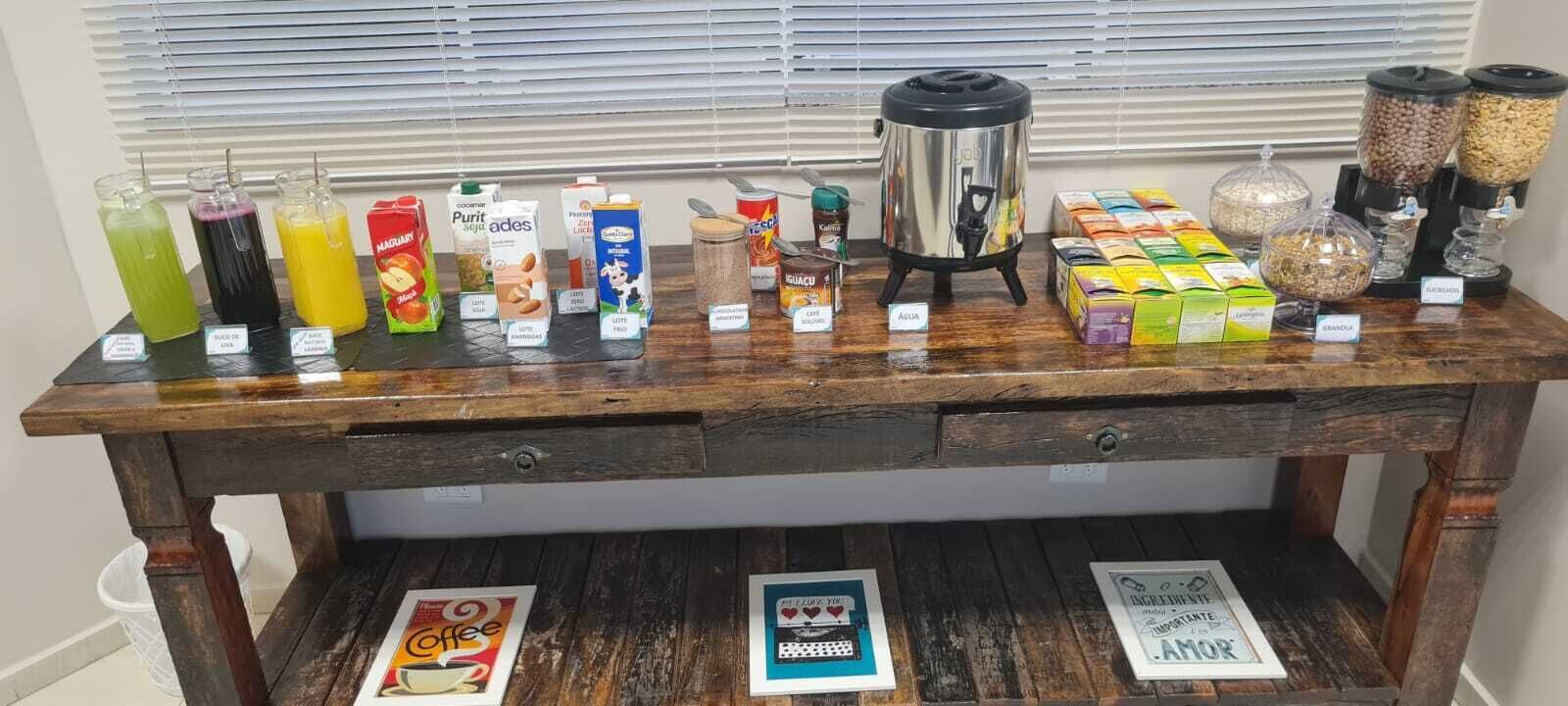 A wooden table with various food and drink items, including a coffee maker, jars of nuts, and boxes of granola.