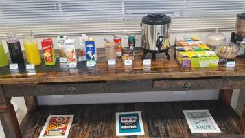 A wooden table with various food and drink items, including a coffee maker, jars of nuts, and boxes of granola.