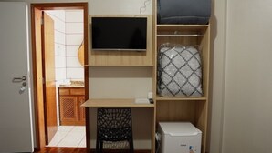 A compact room with a television, a small desk, a chair, and a storage unit. - Hotel LF by Feliciano Joaçaba (Joaçaba)