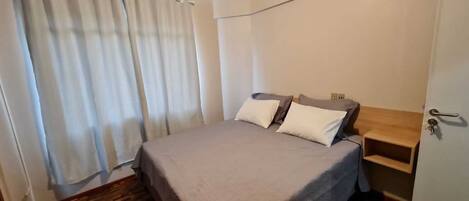 A bedroom with a bed, two pillows, a wooden nightstand, and a door with a keyhole.