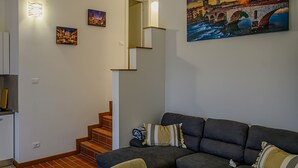 Una sala de estar con un sofá gris oscuro, un cuadro de un puente y una escalera que lleva a otra habitación.