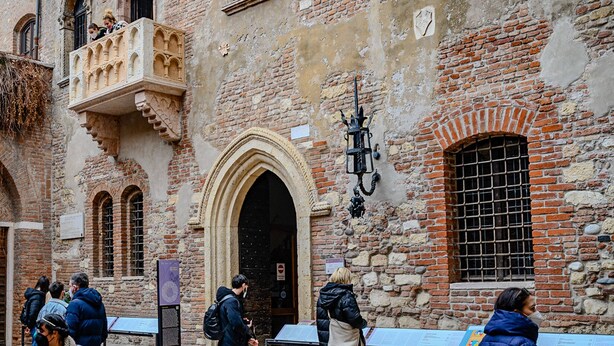 Un edificio histórico con una entrada arqueada destacada, un balcón con elaborados detalles de piedra y un farol tradicional.