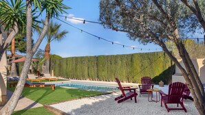 A pool area with red Adirondack chairs and a small table, surrounded by a white gravel border and green grass. - Villa Elia : Cinema : Gym : KidsRoom : Pool & BBQ (La Eliana)