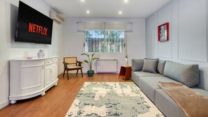 A living room with a flat-screen TV, a sofa, a cabinet, a plant, and a window with a view of trees. - Villa Elia : Cinema : Gym : KidsRoom : Pool & BBQ (La Eliana)