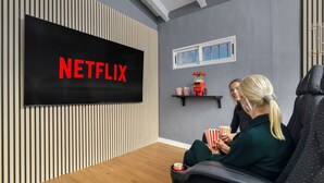 A modern living room with a large flat-screen TV displaying the Netflix logo, wooden paneling, a window, and a popcorn machine. - Villa Elia : Cinema : Gym : KidsRoom : Pool & BBQ (La Eliana)