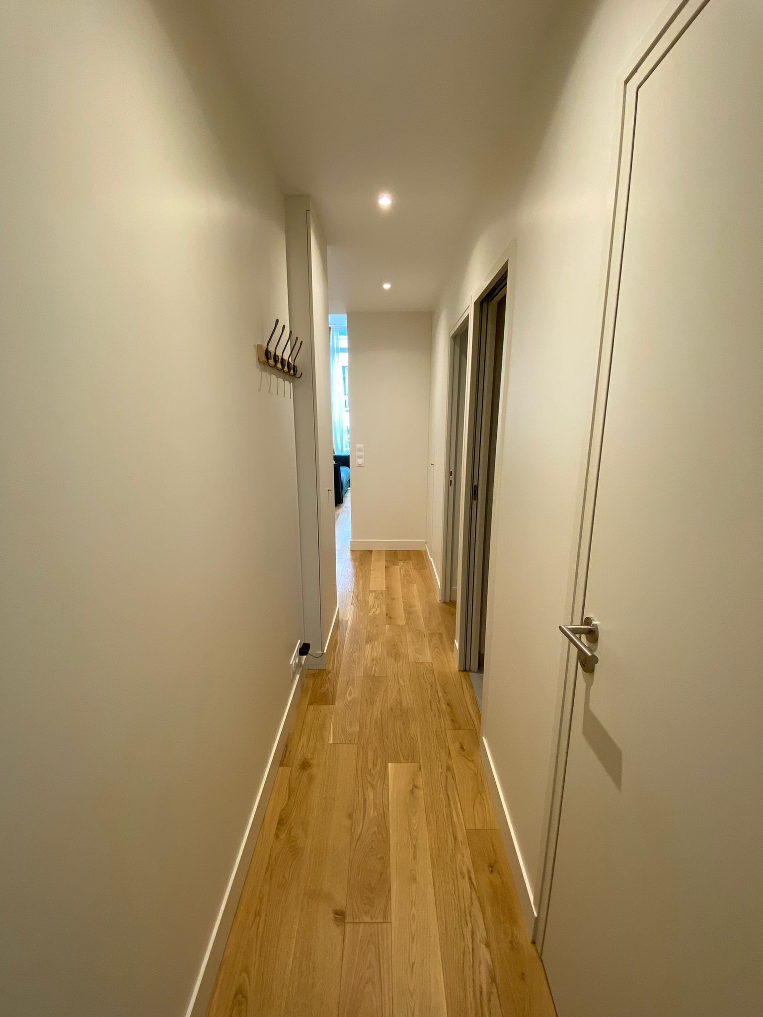 A narrow hallway with wooden flooring, white walls, and a door on the right.