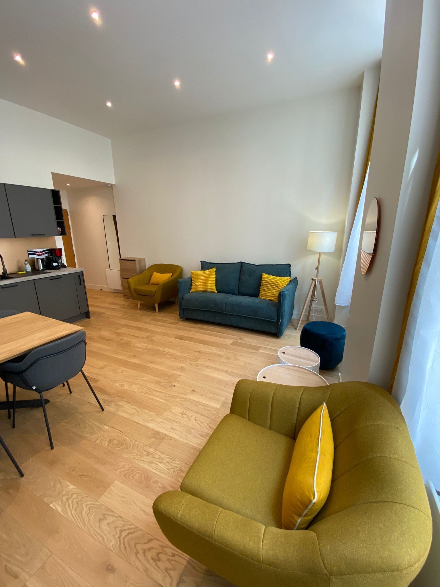 Ein modernes Wohnzimmer mit einer Couch, einem Esstisch mit Stühlen und einer Küche im Hintergrund.