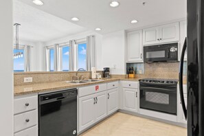 A modern kitchen with white cabinets, a granite countertop, a dishwasher, a microwave, and an oven. - Treasure Shores3br Beachfront Corner Unit Sleeps 8 With Stunning Gulf Views! (Panama City Beach)