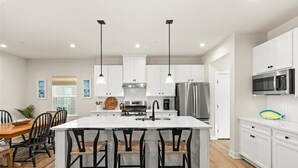 A modern kitchen with white cabinetry, stainless steel appliances, and a central island with bar stools.