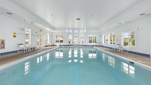 A large indoor swimming pool with clear blue water, surrounded by white walls and large windows.